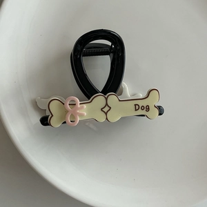 Détail d'une pince à cheveux chien noire avec os beige et petit nœud rose mignon
