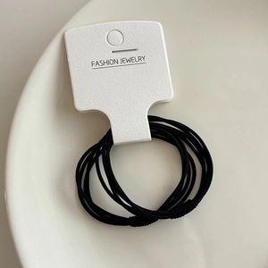 Détail d'un lot d'élastiques à cheveux noirs sur un plateau en céramique blanche