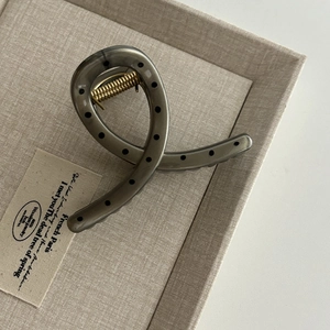 Detail view of large grey polka dot hair claw clip with golden metal spring on beige fabric