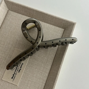 Close-up of a large translucent grey hair claw clip with black polka dots and gold spring
