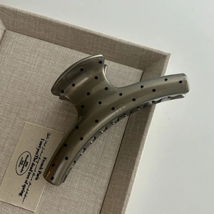 Macro view of a grey hair claw clip with black polka dots on a beige textured tray
