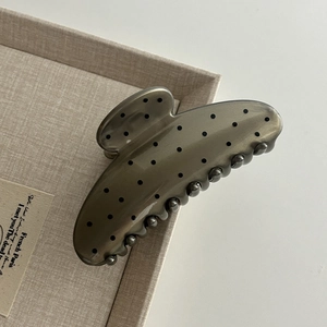 Elegant large translucent grey hair claw clip with black polka dots on a display tray