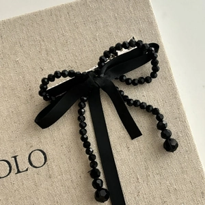 Barrette nœud en perles noires avec rubans de satin et glands sur un coffret beige