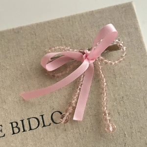 Détail de pince à cheveux avec nœud en ruban rose et perles transparentes sur boîte