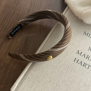 Close-up of brown striped headband with gold heart detail and handmade label