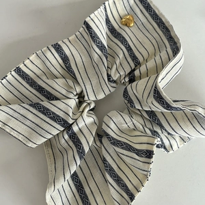 Detail of blue striped oversized scrunchie with a gold heart pendant and geometric patterns