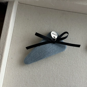 Détail de la barrette BB en denim avec nœud en ruban noir et breloque en métal Love