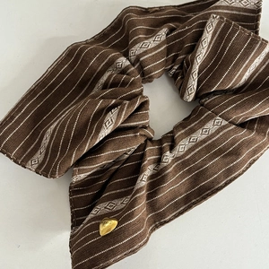 Detailed texture of brown striped fabric scrunchie with golden heart metal charm