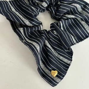 Detailed macro view of navy striped scrunchie fabric with engraved golden heart charm
