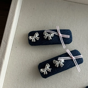 Détail de la pince à cheveux en denim avec nœuds métalliques et ruban rose