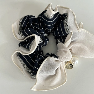 Detail of striped black scrunchie with faux pearl and golden logo metal pendant