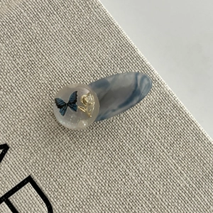 Vue macro d'une pince à cheveux en acétate bleue avec sphère en résine et motif papillon