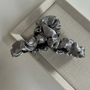 Gros plan d'une pince à cheveux fleur argentée avec texture métallique plissée sur plateau