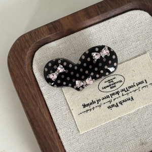 Vintage black polka dot hair clip with three pink rhinestone bows on wooden tray