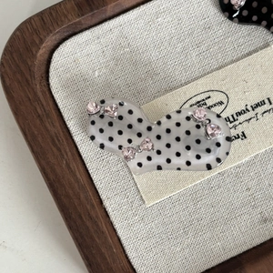 Detailed view of polka dot bow hair clip with pink heart rhinestones on linen fabric