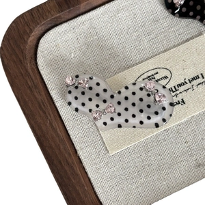 Polka dot heart hair clip with pink rhinestones on a beige linen display tray