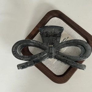 Detail of a large bow hair claw clip in acetate with dark ink texture and glossy finish