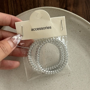 Two metallic silver spiral telephone cord hair ties in minimalist packaging on a ceramic plate