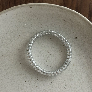 Macro detail of metallic silver spiral hair tie on a minimalist ceramic plate