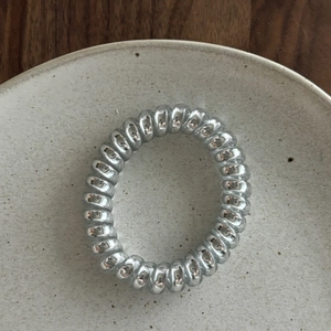 Detailed view of a silver spiral telephone wire hair tie on a rustic ceramic plate