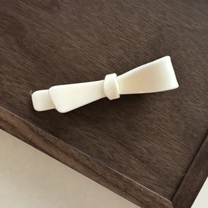Detail view of a white resin butterfly hair clip resting on a dark wood surface