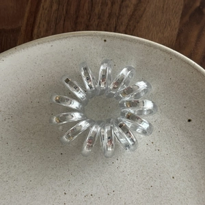 Close-up of a clear spiral hair tie placed on a ceramic plate with wood background