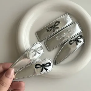 Detailed set of 5 silver PU leather hair clips with rhinestone bows in a ceramic dish