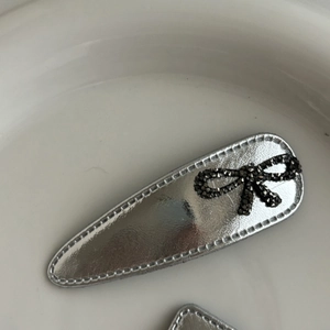 Macro detail of silver mirror leather drop hair clip with black rhinestone bow decoration