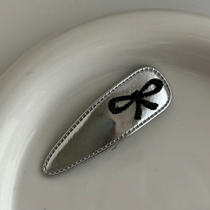 Close-up of silver faux leather hair clip with black rhinestone bow detail on white plate