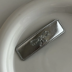 Detail of silver metallic hair clip with rhinestone bow and stitching on ceramic plate