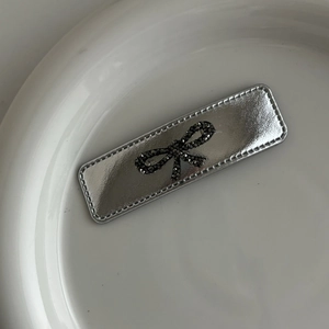 Silver metallic leather hair clip with a dark rhinestone bow design on a ceramic plate