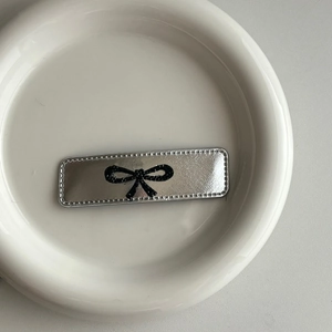 Silver leather bow hair clip with sparkling rhinestones in a white ceramic dish