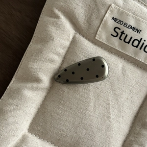 Detail einer tropfenförmigen Haarspange mit schwarzen Punkten auf dunkelgrauem Metall