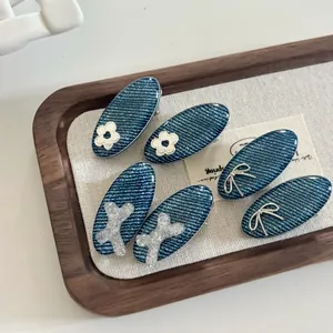 Detail of 6-piece denim blue bow hair clips with silver metallic accents on a tray