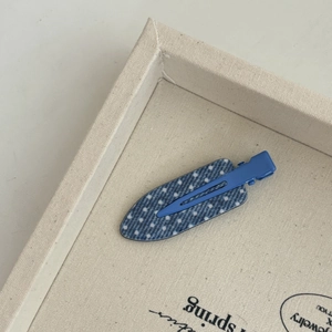 Macro detail of blue polka dot seamless hair clip on a minimalist textured beige tray