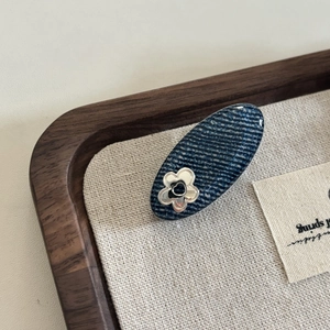 Close-up of denim fabric hair clip with a silver flower on a wooden tray background