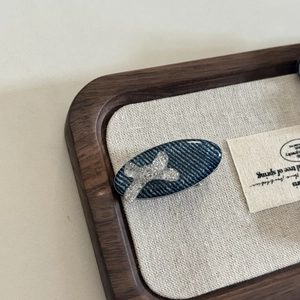 Denim blue oval hair clip with sparkling silver bow detail on a vintage wood tray
