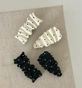 Close-up of four wavy polka dot hair clips in black and cream on a linen book cover