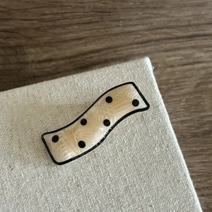 Detail view of wavy cream acetate hair clip with black polka dots on display stand