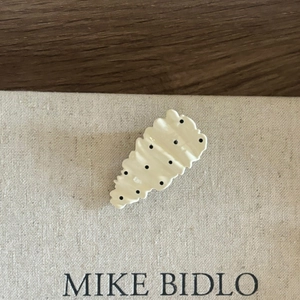 Chic cream wavy hair clip with black polka dots on a minimalist linen background