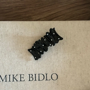 Detail of black wavy hair clip with white polka dots on a textured card display