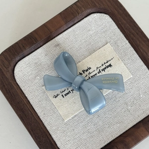 Elegant haze blue acetate bow hair clip with gold lettering on a vintage textured fabric