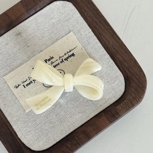 Elegant cream white acetate bow hair clip with French gold lettering on a linen background