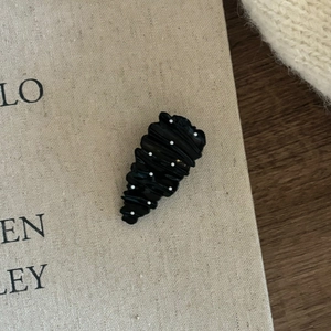 Detail view of black wavy hair clip with white polka dots on textured canvas background