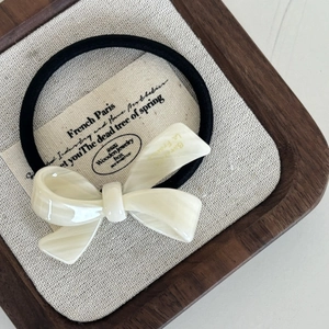 Detail view of a cream acetate bow hair tie with marble texture on a rustic wooden tray