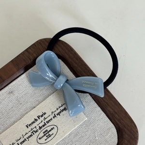 Close-up of misty blue acetate bow hair tie with gold lettering on a rustic wooden tray