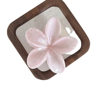 Pink marble texture frangipani flower hair claw clip displayed on a wooden tray