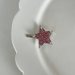 Detailaufnahme einer silbernen Sternen-Haarklammer mit rosa Strass auf weißem Porzellan