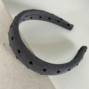 Close-up of grey padded bow headband with black heart pattern on textured fabric