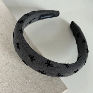 Close-up of handmade grey fabric headband with black bow embroidery and thick padded design